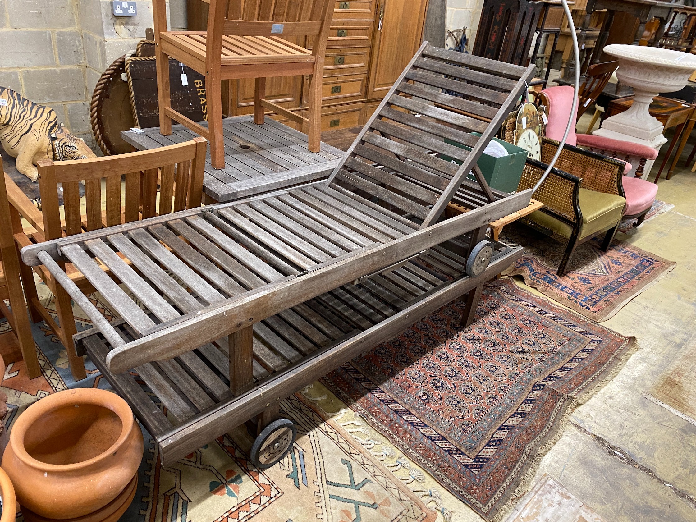 A pair of weathered teak garden loungers and a small folding teak table